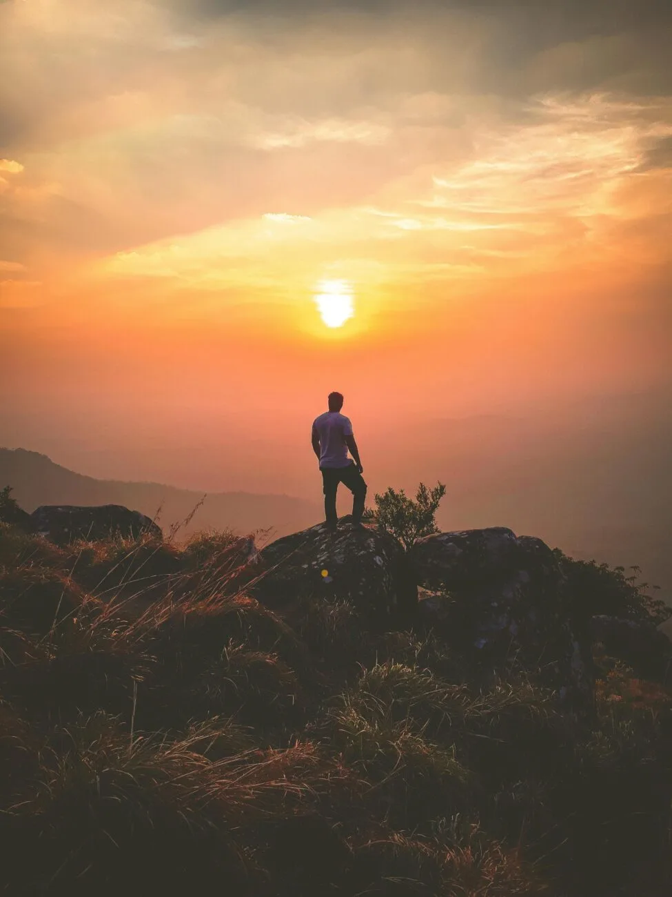 Un homme debout sur une montagne regardant le soleil se couchant